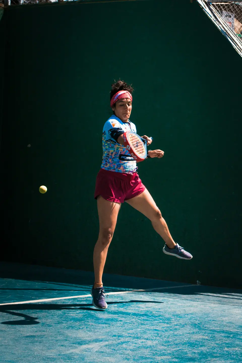 A player driving a forehand across the court in front of a green wall.